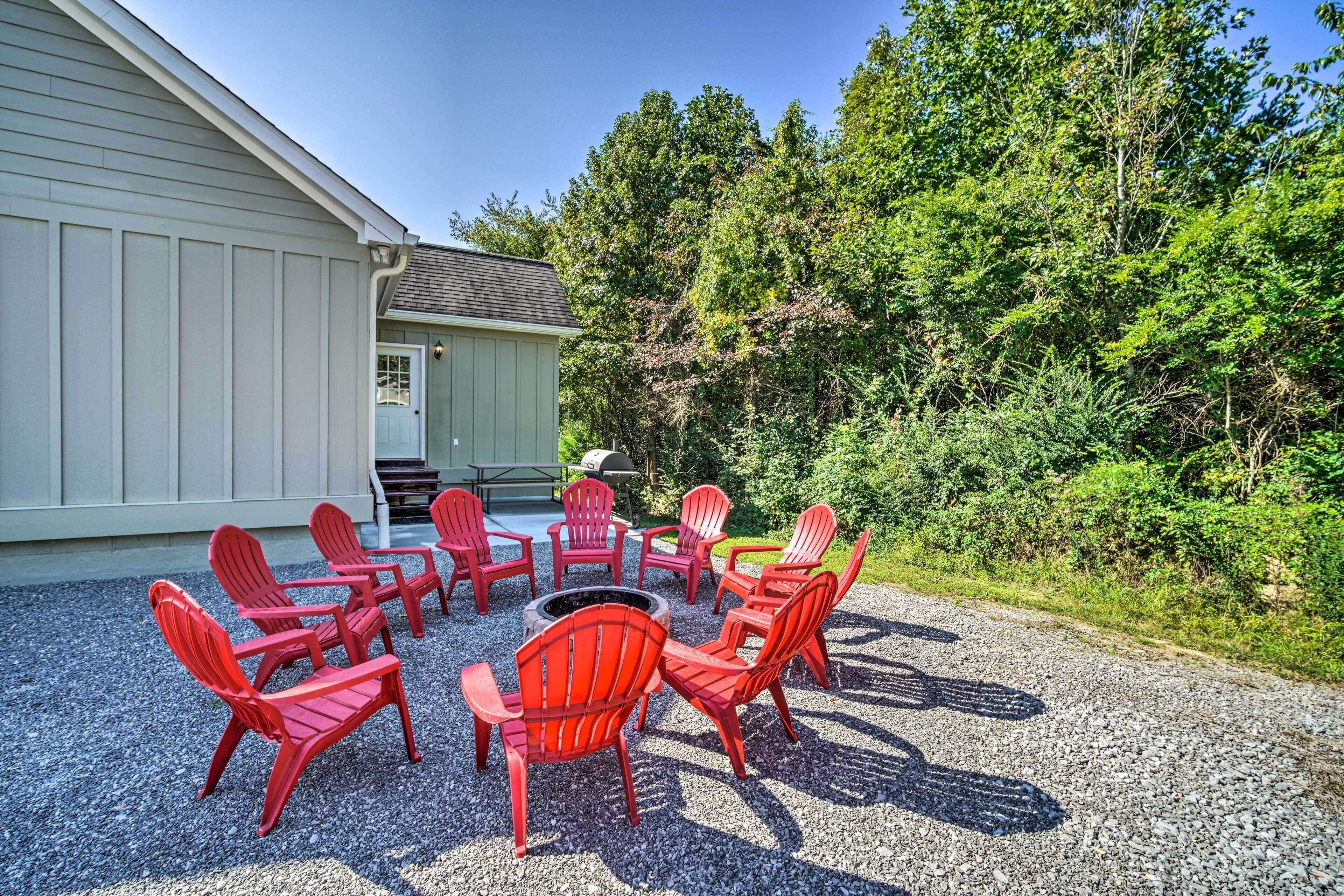 A circular outdoor seating area with red chairs and a fire pit, surrounded by gravel, with a building and trees in the background.