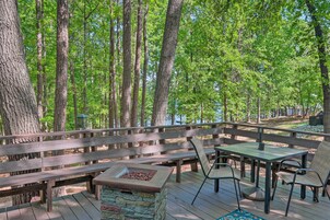 A wooden deck with a stone fire pit, wooden benches, and metal chairs.