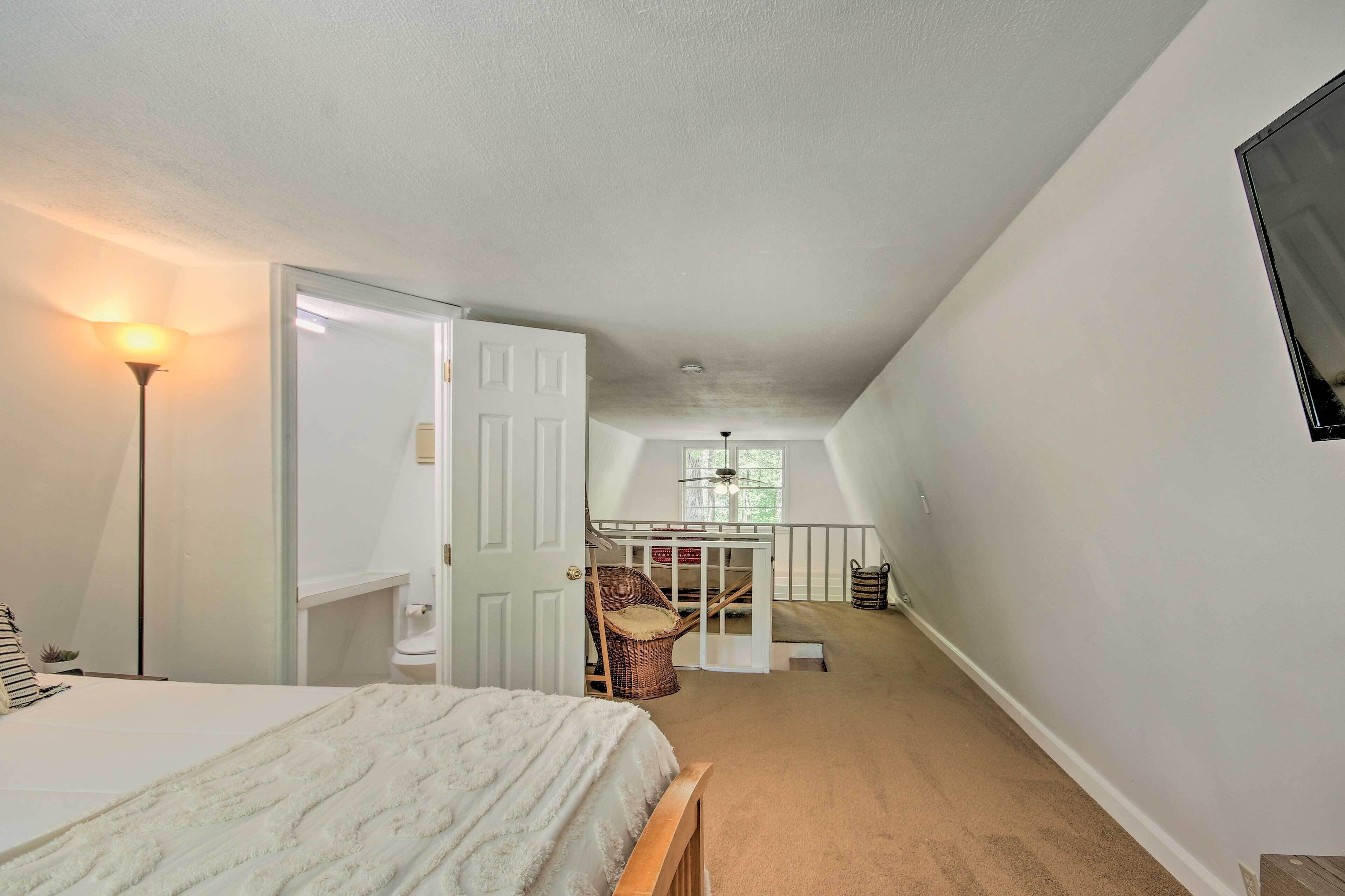 A bedroom with a bed, a chair, a desk, and a staircase leading to an upper level.