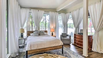 A bedroom with a bed, bedside tables, a chair, a dresser, and large windows with curtains.