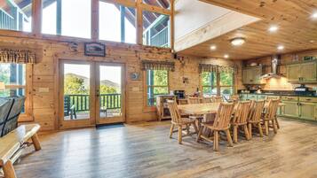 A wooden cabin interior with a dining area, kitchen, and large windows.