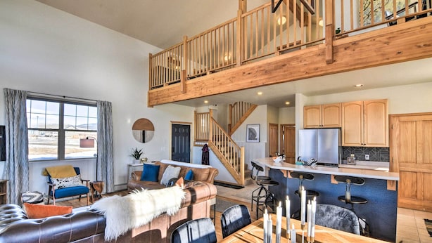A spacious living area with a high ceiling, a wooden staircase, a kitchen with wooden cabinets, and a dining area with a table and chairs. - 503 Mountain Loft w/ Views: 1 Mi to Dwtn Fairplay! (Fairplay)