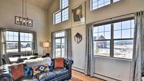 A spacious living room with a leather sofa, a wooden coffee table, and large windows offering a view of the outdoors. - 503 Mountain Loft w/ Views: 1 Mi to Dwtn Fairplay! (Fairplay)