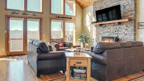 A spacious living room with a stone fireplace, leather sofas, and large windows offering a view of the mountains. - Pool, Hot Tub & Mountain Views: Cleveland Cabin (Cleveland)