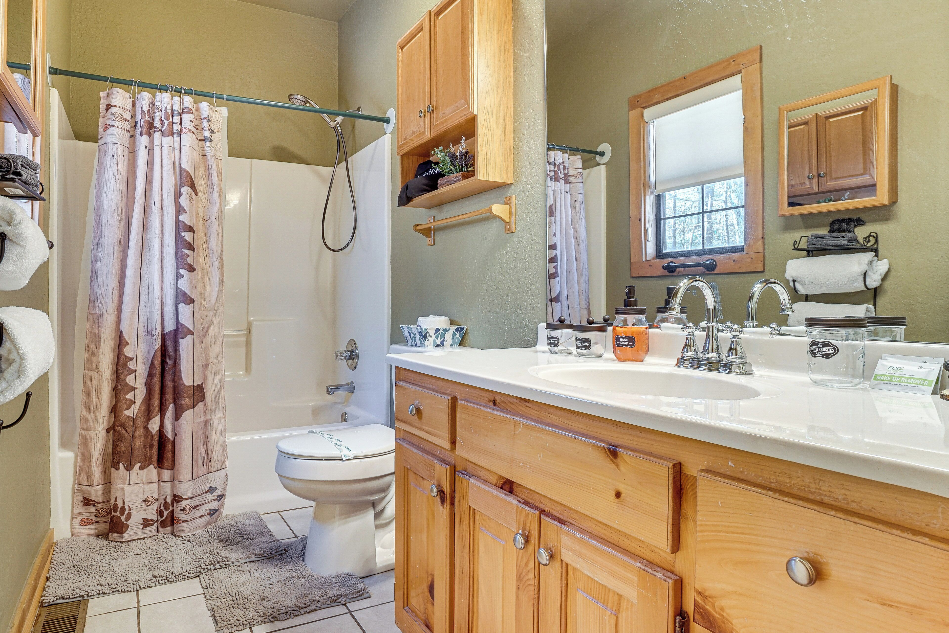 A bathroom with a wooden vanity, a toilet, a shower with a curtain, and a window.