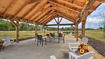 A covered outdoor seating area with Adirondack chairs and a table, surrounded by a wooden pavilion with a view of a lake and greenery.
