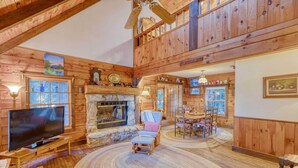 A log cabin interior with a fireplace, television, dining area, and a large window.