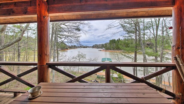 A wooden deck with a metal bowl on a coaster, overlooking a river and trees.