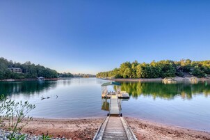 A calm lake with a wooden dock leading to a covered seating area.
