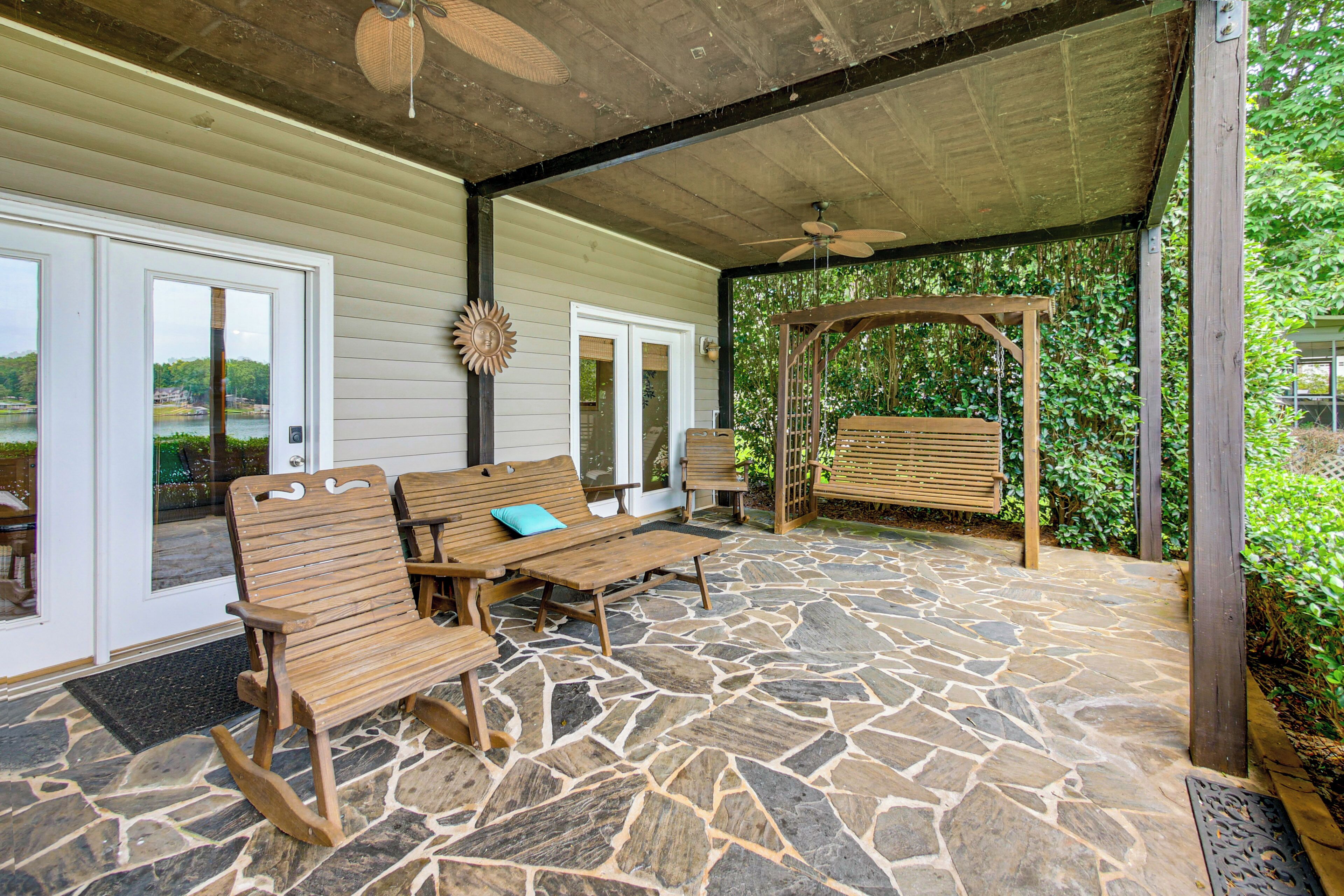 Eine überdachte Terrasse mit Steinboden, Holzbanken und einer Pergola.