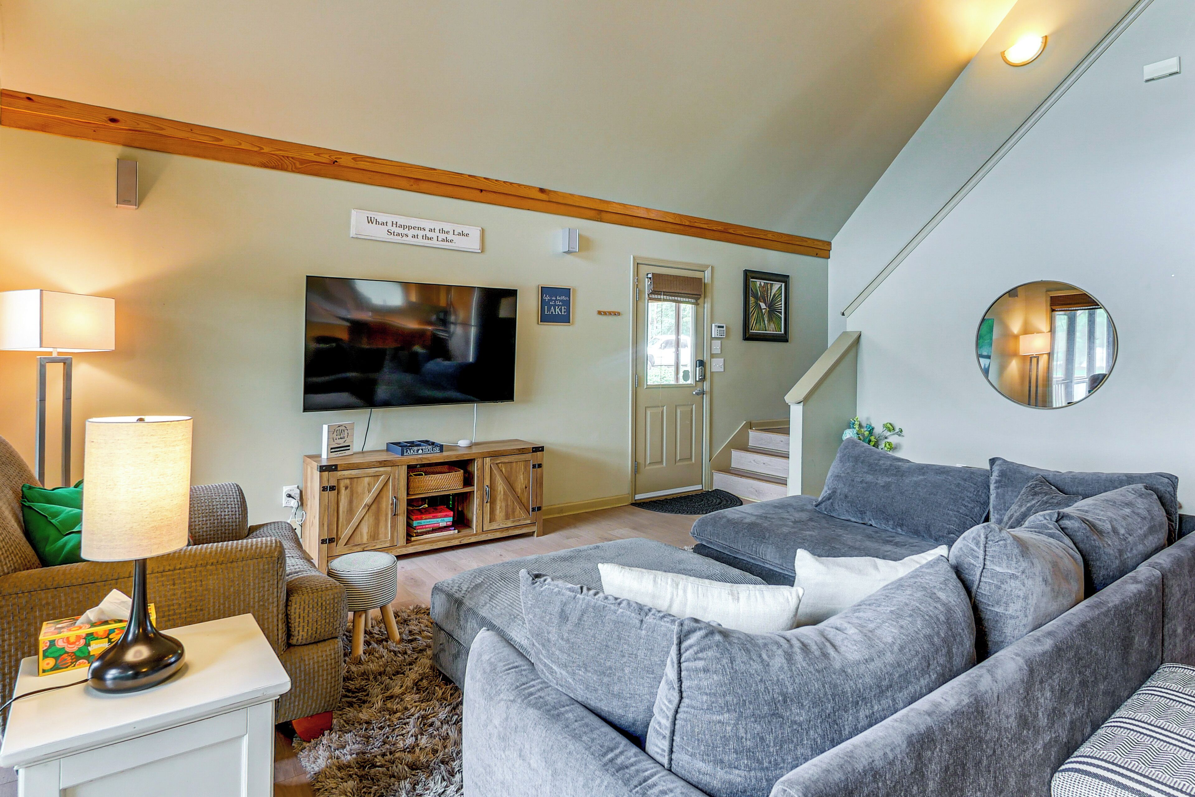 A living room with a television, grey sofas, a wooden cabinet, and a staircase.