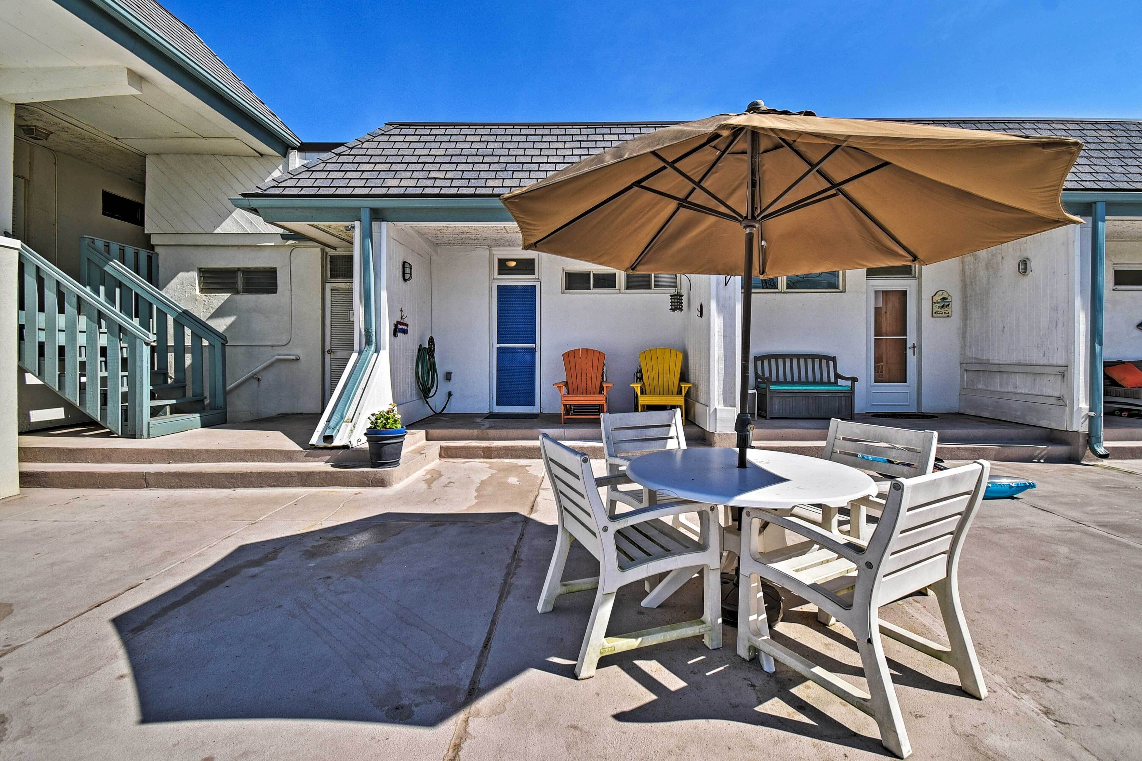A patio area with a table and chairs, a large umbrella, and a staircase leading to an upper level.