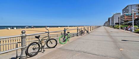 A coastal promenade with bicycles parked along the railing, a clear sky, and buildings in the background.