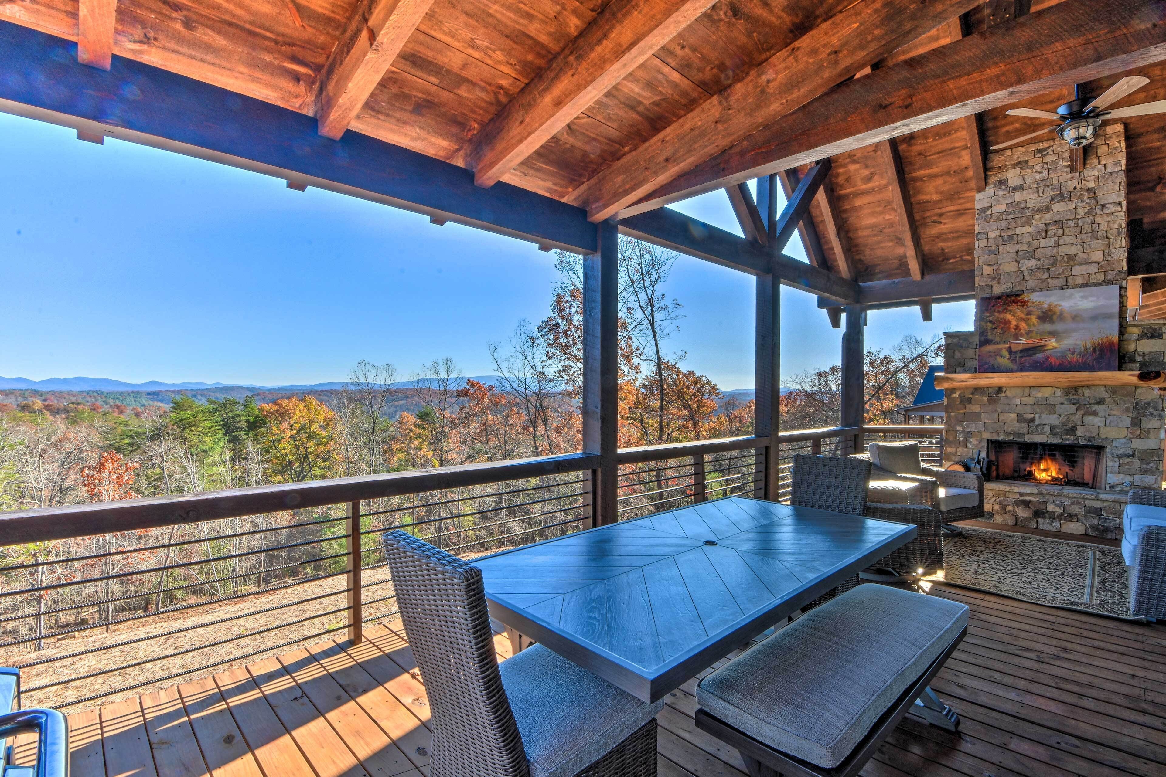A wooden deck with a stone fireplace, outdoor seating, and a scenic view.
