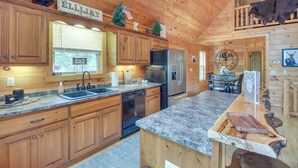 A wooden cabin kitchen with granite countertops, stainless steel appliances, and a dining area with a chandelier. - Upscale Coosawattee Cabin w/ Hot Tub & Fire Pit! (Ellijay)