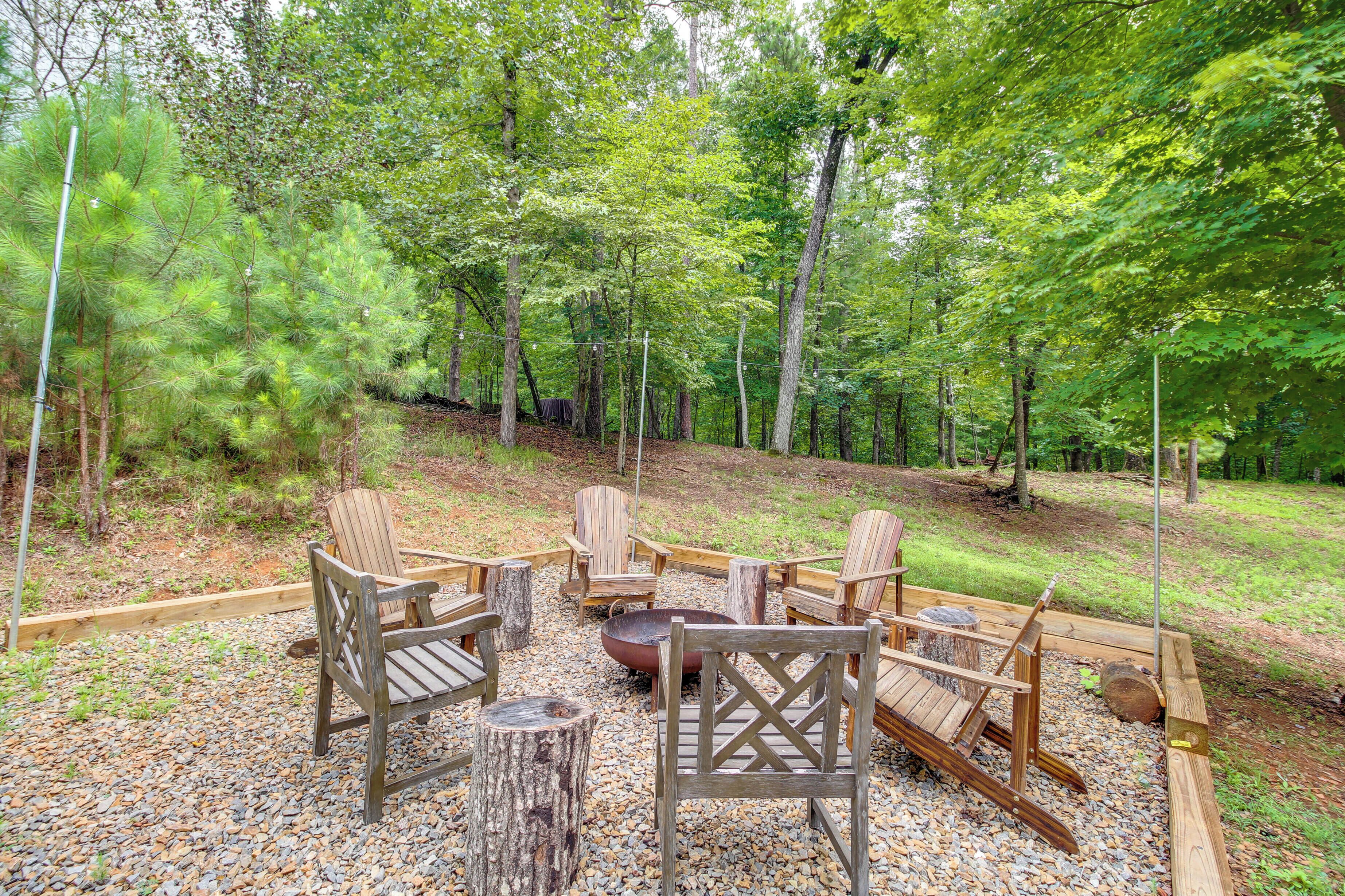 A wooden deck with Adirondack chairs and a fire pit surrounded by a forest.