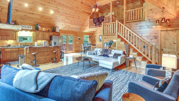 A spacious log cabin with a large living area, a kitchen, and a staircase leading to a loft. - Upscale Coosawattee Cabin w/ Hot Tub & Fire Pit! (Ellijay)