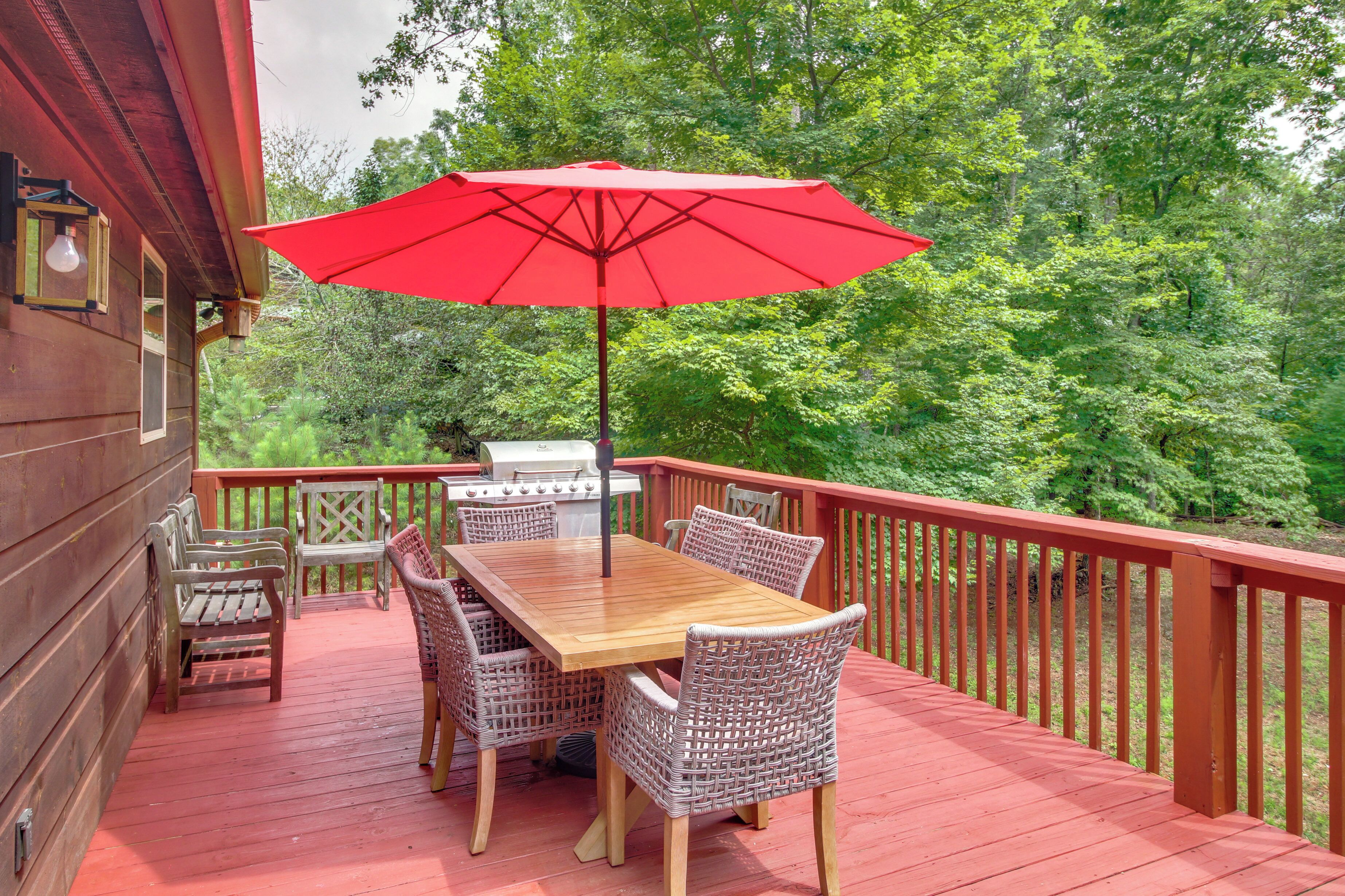 A wooden deck with a red umbrella, wicker chairs, and a wooden table.