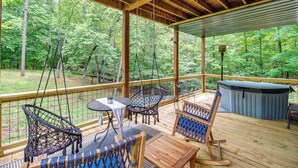 A covered outdoor deck with wooden furniture, including chairs and tables, overlooking a forested area. - Upscale Coosawattee Cabin w/ Hot Tub & Fire Pit! (Ellijay)