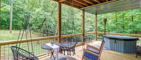 A covered outdoor deck with wooden furniture, including chairs and tables, overlooking a forested area.