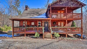 A two-story log cabin with a balcony, a front porch, and a chimney. - Upscale Coosawattee Cabin w/ Hot Tub & Fire Pit! (Ellijay)
