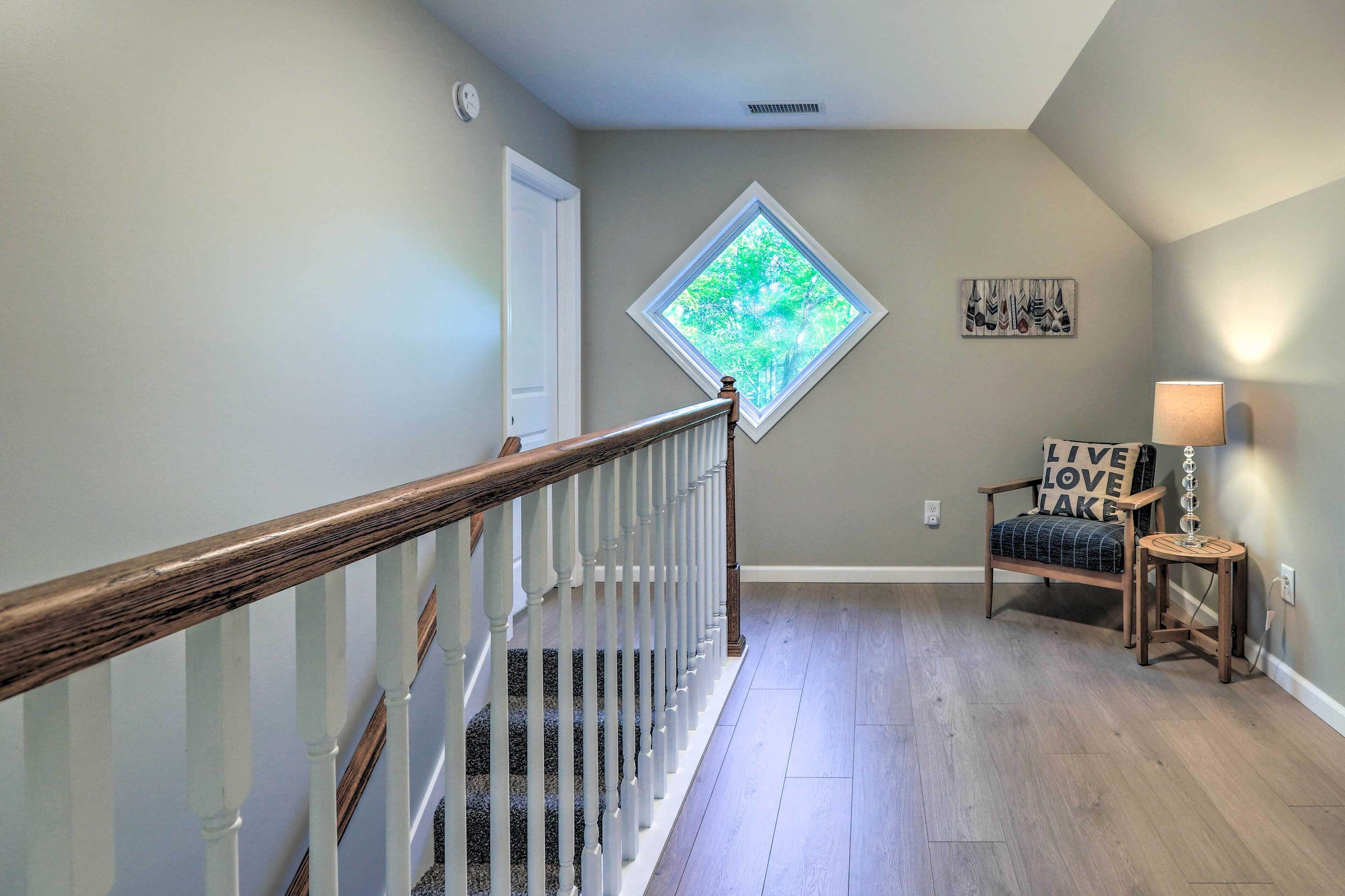 A staircase with a wooden handrail leading to a landing. A window with a diamond frame and a view of trees is visible on the landing wall.