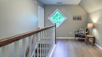 A staircase with a wooden handrail leading to a landing. A window with a diamond frame and a view of trees is visible on the landing wall.