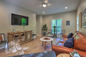 Una sala de estar con sofá de cuero, aparador de madera, televisor de pantalla plana y un comedor con mesa y sillas.