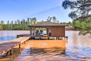 Un muelle de madera que se adentra en un lago, con un área de estar cubierta y un pequeño pabellón.