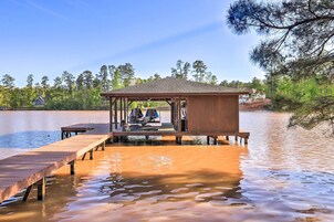 A wooden dock extending into a lake with a covered seating area and a small pavilion.