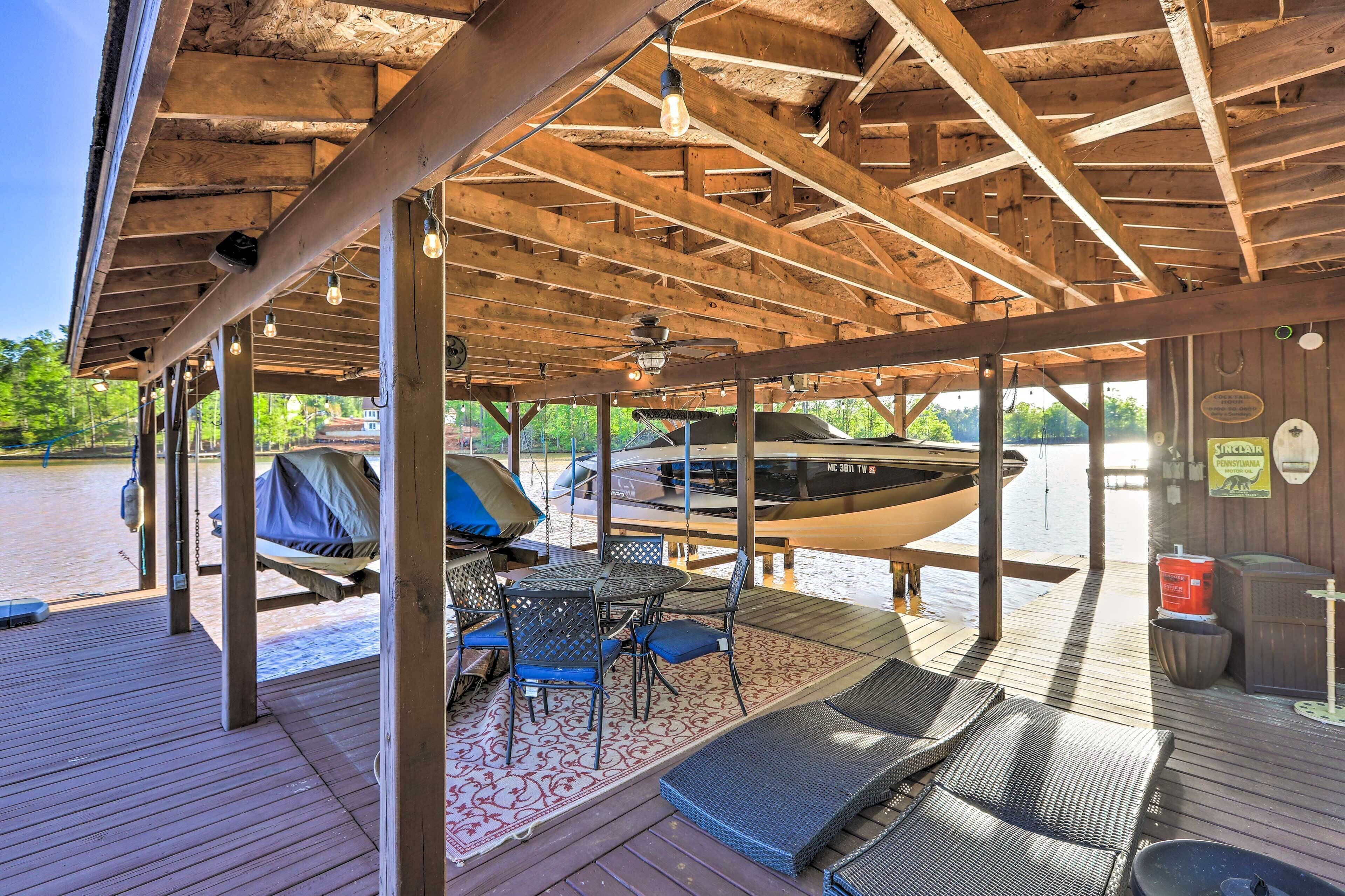 Un espace extérieur abrité doté d’une terrasse en bois, de sièges, d’un barbecue et d’un bateau amarré au fond.