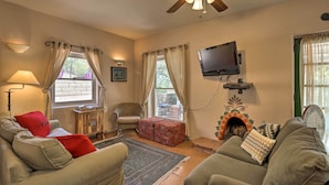 Una sala de estar acogedora con un sofá, sillones, televisor, chimenea y ventilador de techo.
