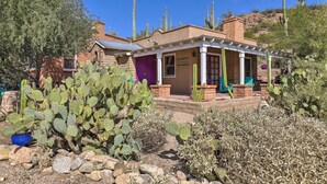 Un edificio con fachada de ladrillo, una puerta morada y un porche cubierto con un jardín de cactus al frente.