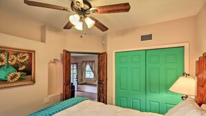 Un dormitorio con cama, ventilador de techo, puerta verde y un cuadro en la pared.