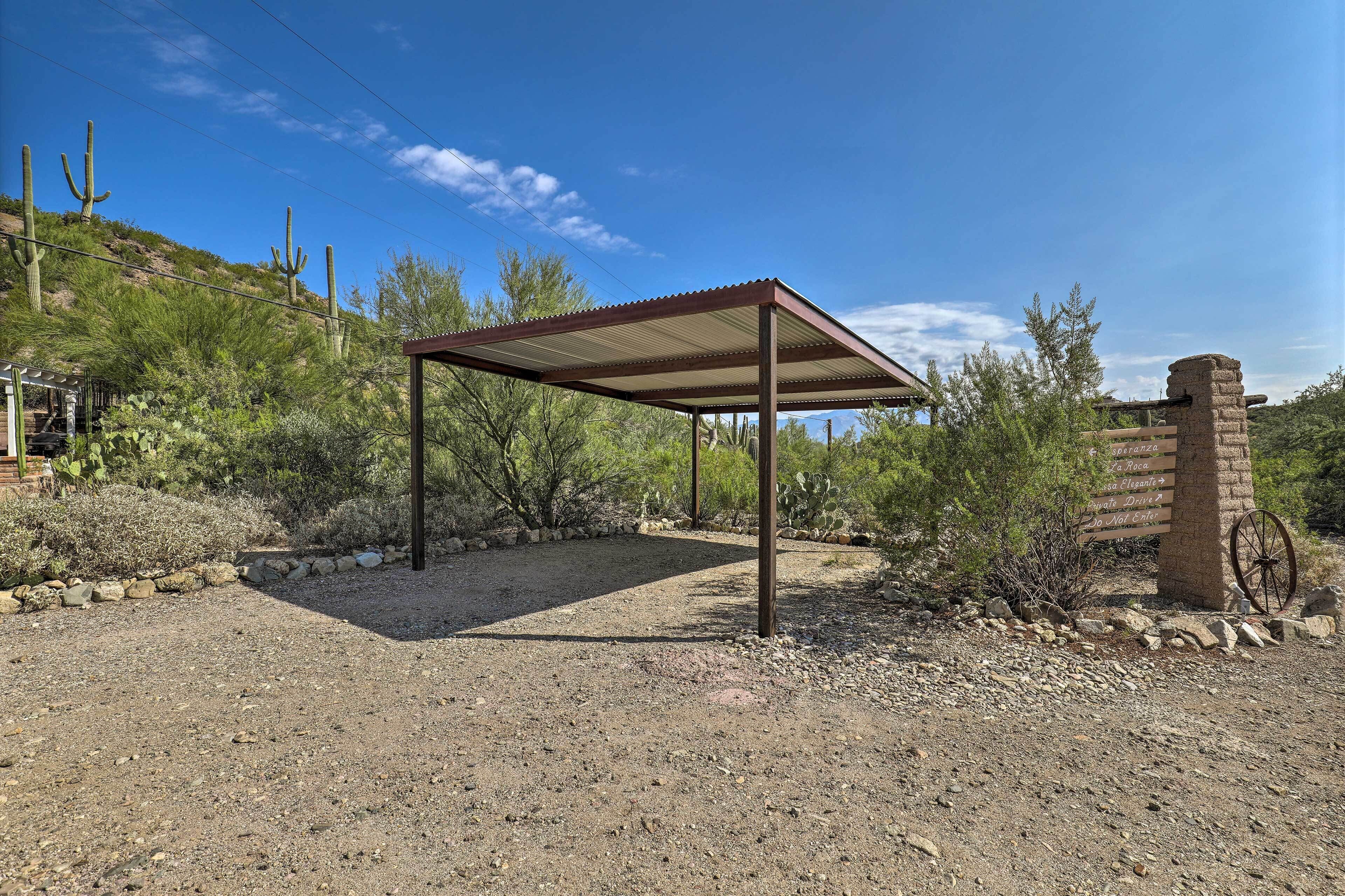 A covered outdoor area with a gravel ground, surrounded by desert vegetation and a stone wall.