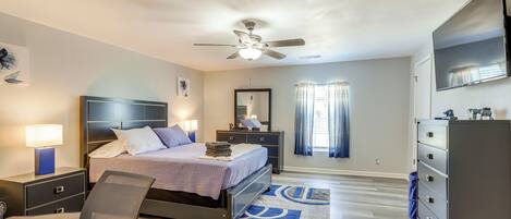 A modern bedroom with a bed, desk, chair, nightstands, dresser, and a ceiling fan.