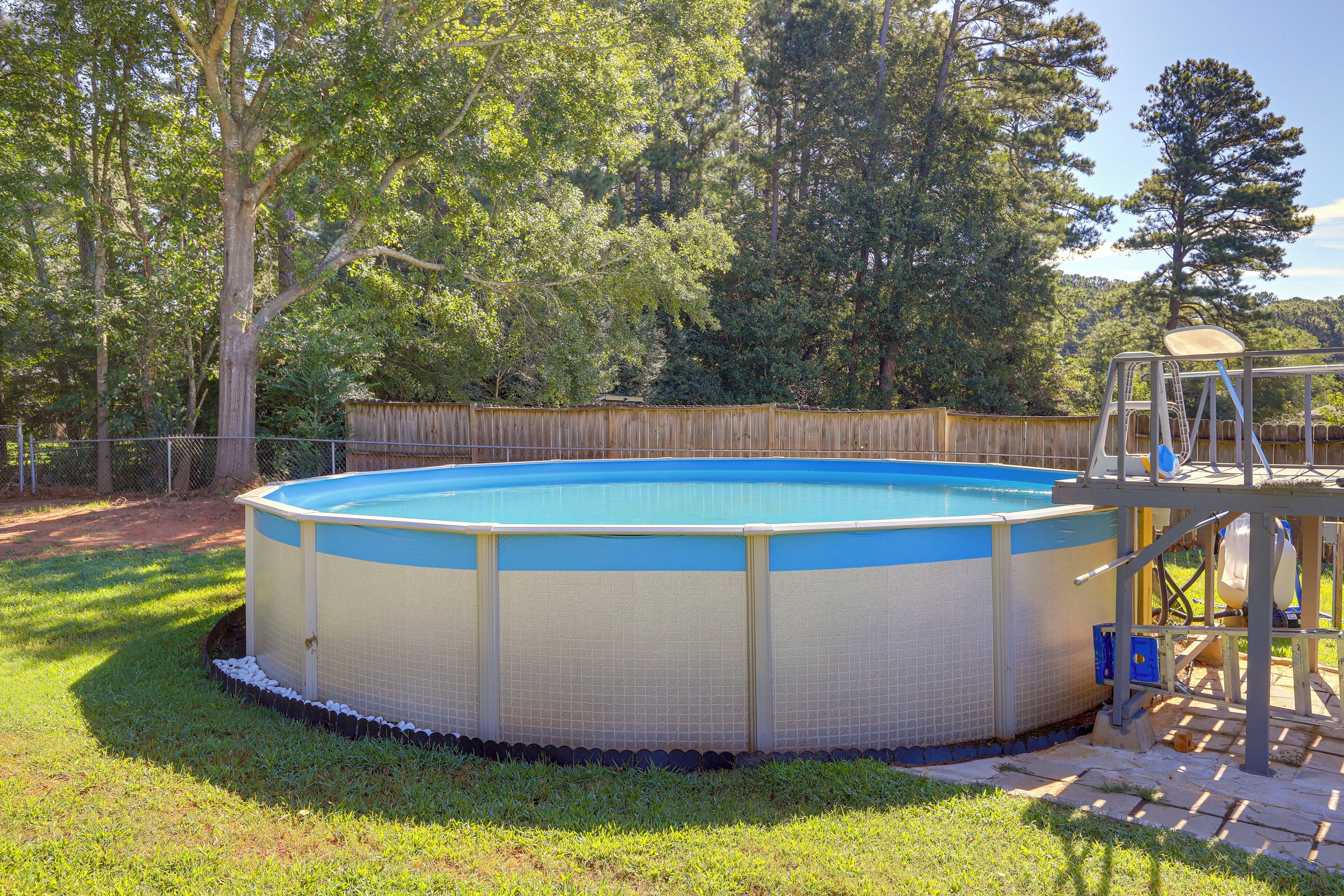 A round above-ground pool with a wooden deck and a ladder, surrounded by a wooden fence and trees.