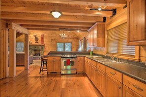 A wooden cabin-style kitchen with a central island, wooden cabinets, and a stone fireplace.