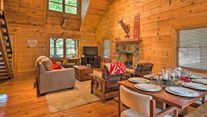 Ein Blockhaus-Interieur mit Kamin, Fernseher, Essbereich für sechs Personen und einer Treppe.