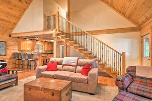 A spacious living area with a wooden staircase, a sofa with red cushions, and a plaid-patterned chair.
