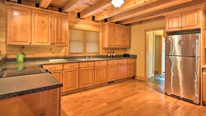 Eine Küche mit Holzschränken, einem Edelstahlkühlschrank, Granitarbeitsplatten und einer Holzbalkendecke.