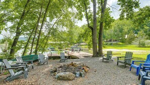 Ein Seeufer-Campingplatz mit Adirondack-Stühlen, einer Feuerstelle und einem Steg, der ins Wasser führt.