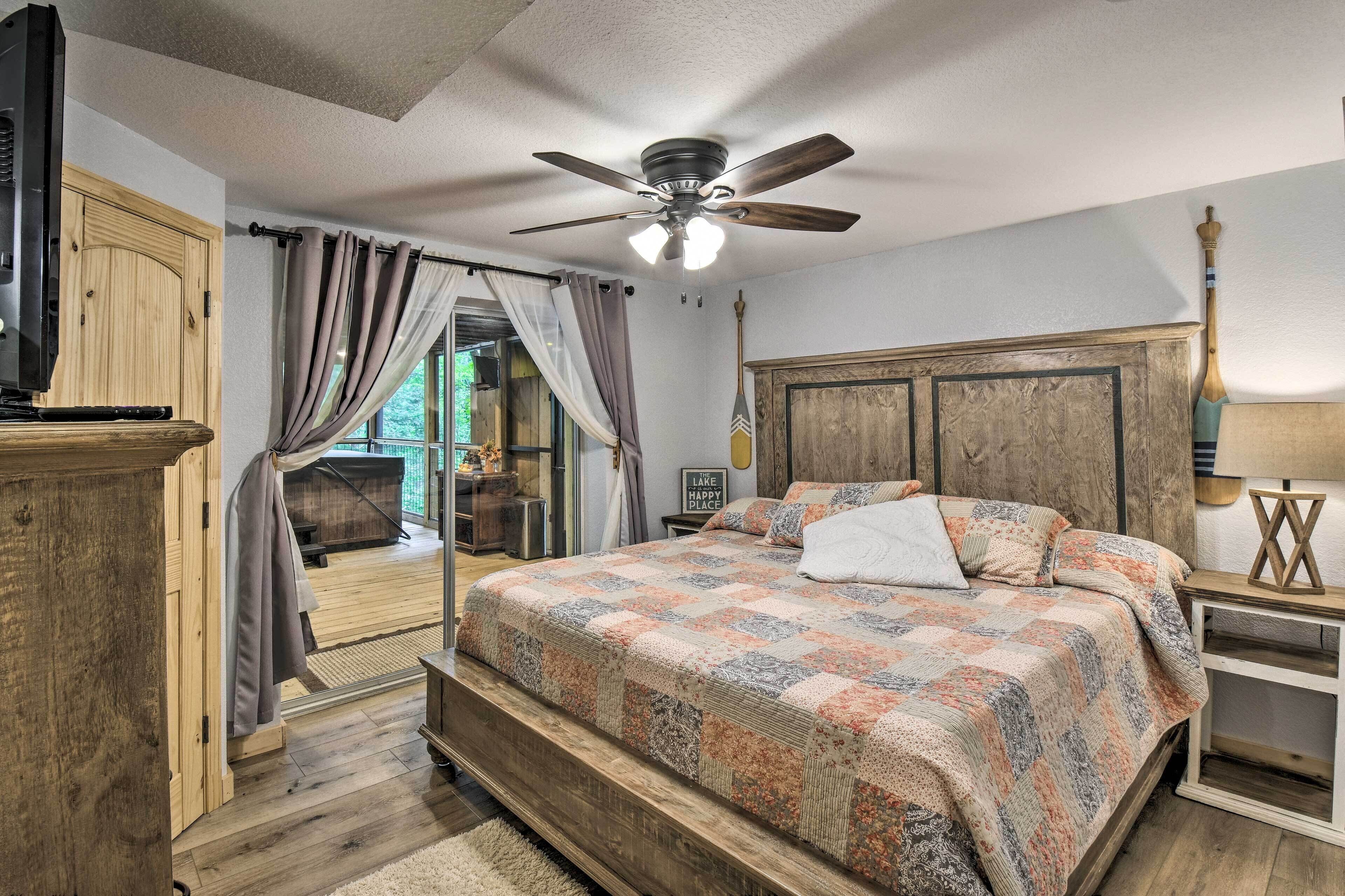 Ein Schlafzimmer mit einem großen Bett, einem hölzernen Kopfteil, einem Deckenventilator und Blick ins Freie durch ein Fenster mit Vorhängen.