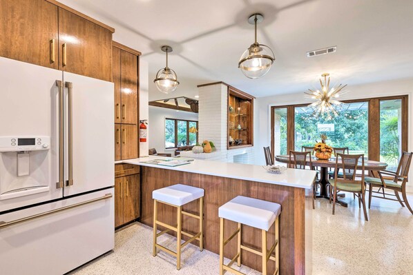 A modern kitchen with a large island, wooden cabinets, stainless steel appliances, and pendant lighting.