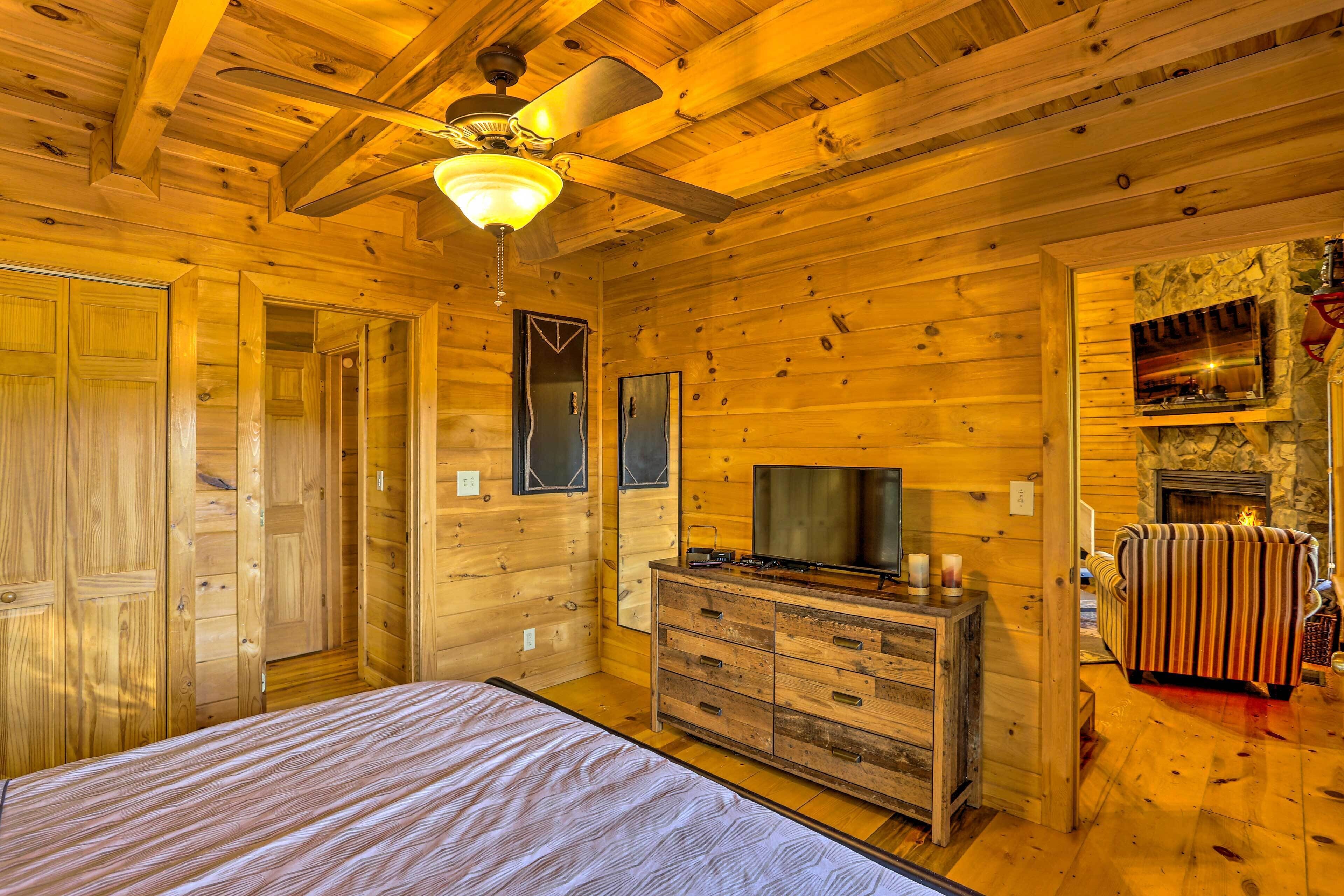A wooden cabin interior with a bed, dresser, television, and fireplace.