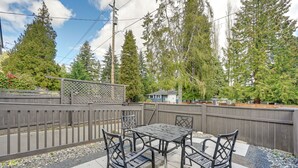 A patio with a metal table and chairs, surrounded by a wooden fence and trees.