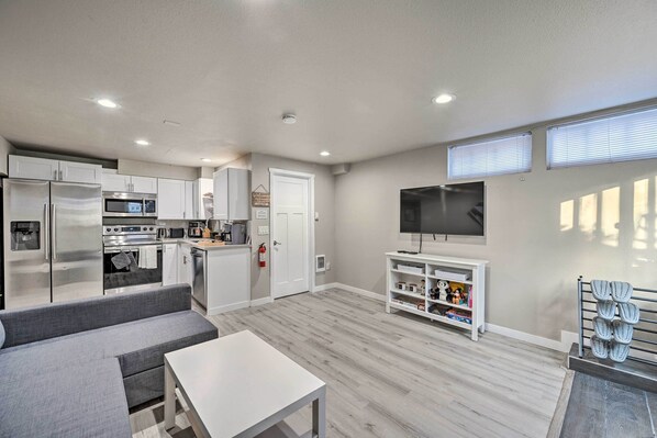 A modern kitchen with stainless steel appliances, a grey sofa, and a flat-screen TV on a white stand. - Family-friendly Seattle Escape: 8 Mi to Dtwn! (Seattle)
