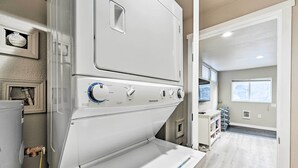 A laundry room with a stacked washer and dryer, a small window, and a door leading to another room.