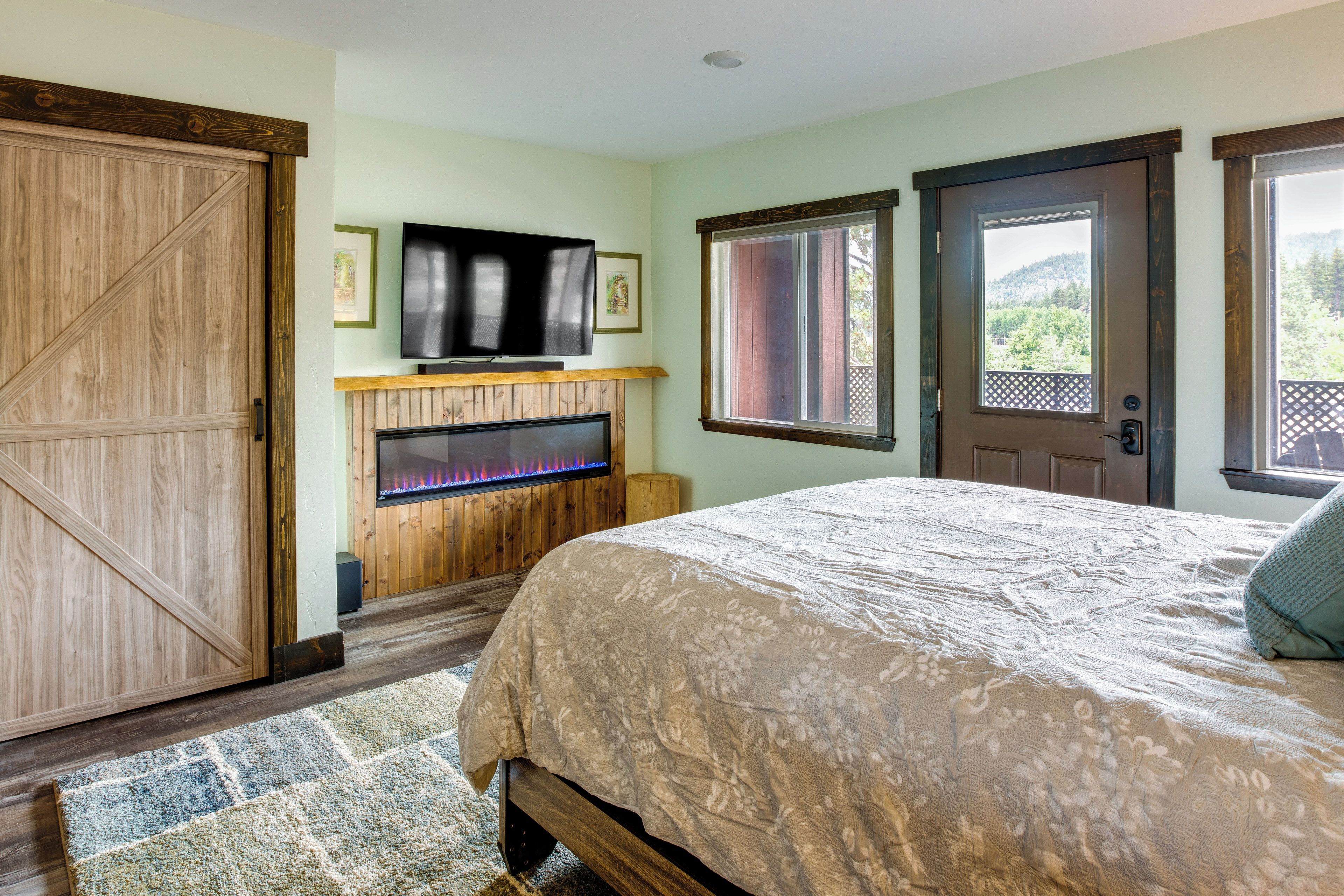 A bedroom with a bed, a fireplace, a television, and a door leading to a balcony.