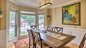 A dining area with a wooden table, chairs, a chandelier, large windows, and a painting on the wall. - Martinez Retreat w/ Seasonal Pool: 9 Mi to Masters (Grovetown)